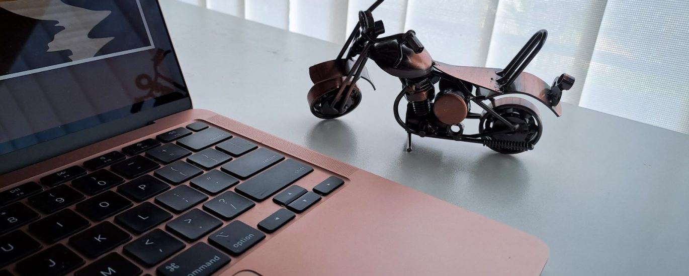 Laptop na radnom stolu pored male metalne makete motocikla