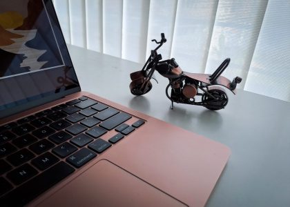 Laptop na radnom stolu pored male metalne makete motocikla